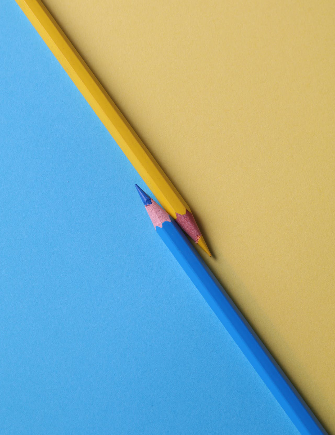A blue and yellow pencil meeting diagonally with their sides respectively coloured