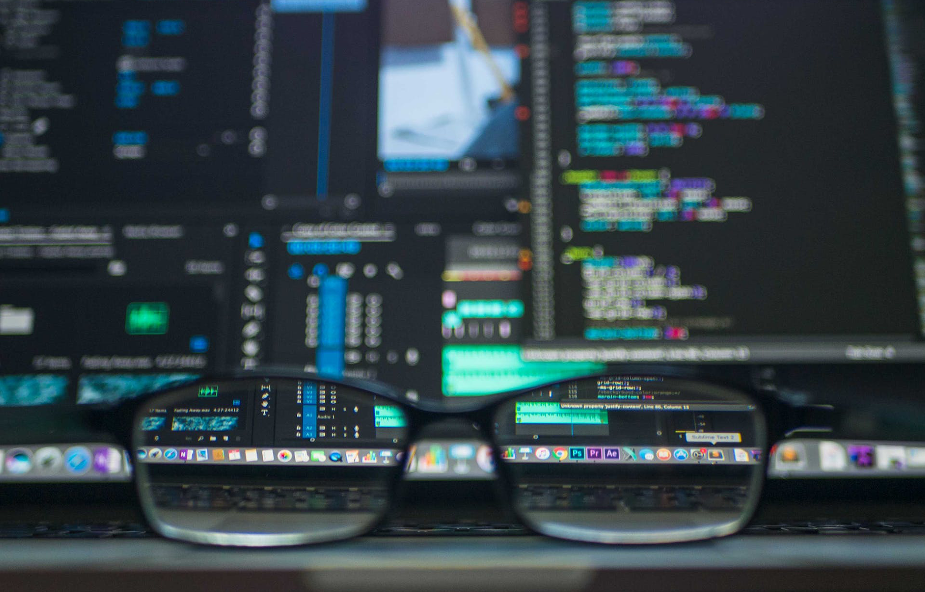 A blurry MacBook with multiple development applications open and glasses sitting on the trackpad which unblur through the lenses